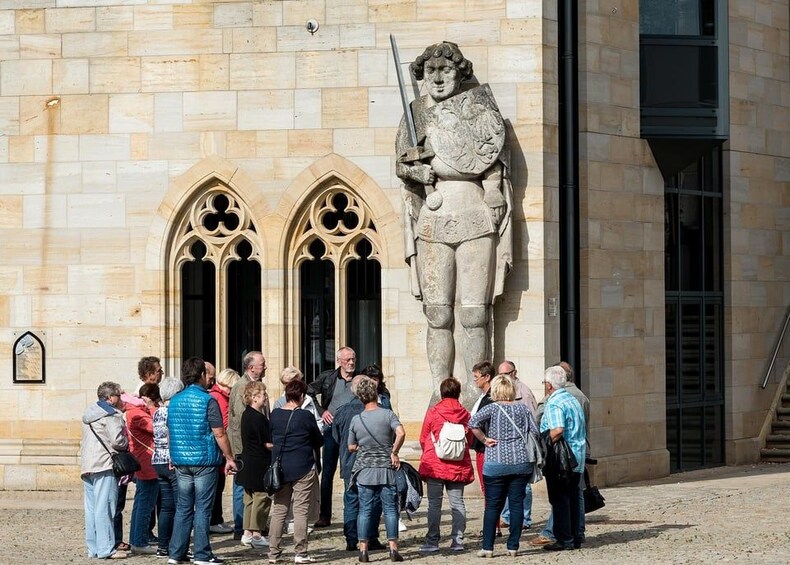 A group of people standing in front of a building with a large statue of a knight. 1