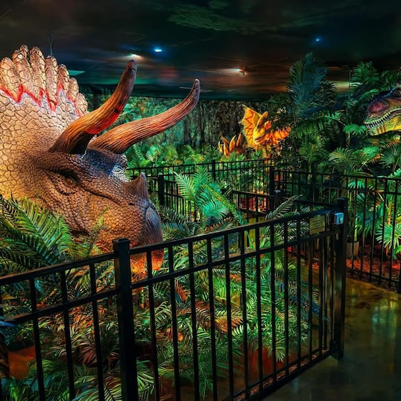 A dinosaur exhibit with a large triceratops and lush green foliage. 1