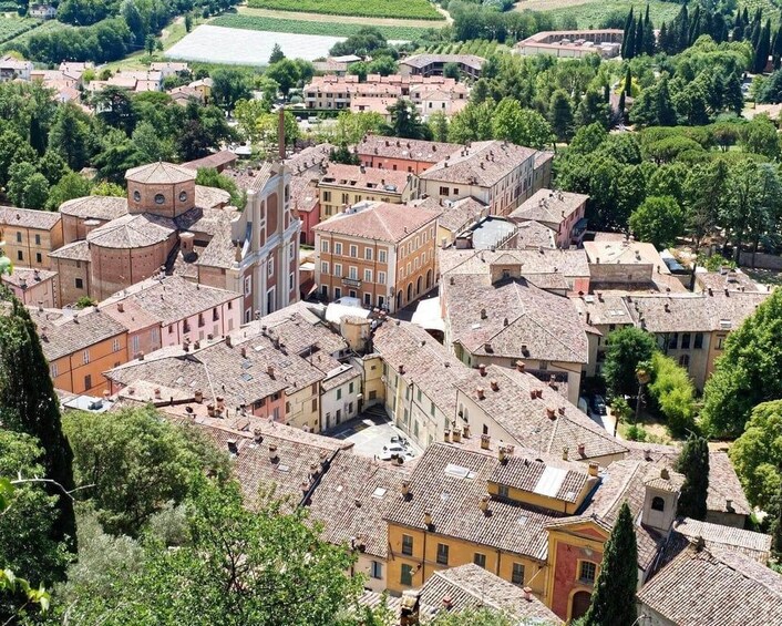A historic town with terracotta-roofed buildings, a prominent church with a dome, and surrounding greenery. 1