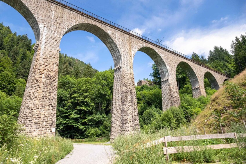 A stone viaduct with multiple arches, surrounded by lush greenery and a clear sky. 5