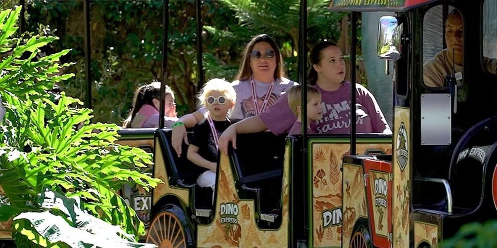 A small train with dinosaur-themed decorations, passengers, and greenery in the background. 5