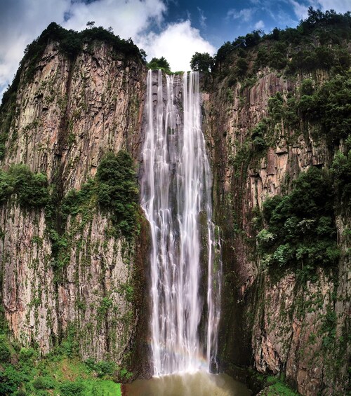 A multi-tiered waterfall cascading down a rocky cliff surrounded by lush greenery. 2