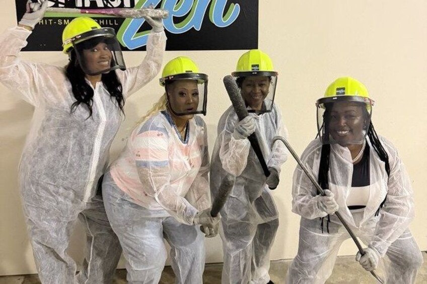 Four people in protective suits and helmets, holding paint rollers, in front of a sign. 3