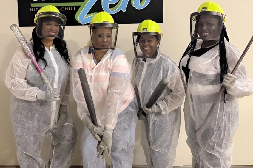 Four people in protective suits holding tools, standing in front of a sign with the word 'Zero' on it. 1