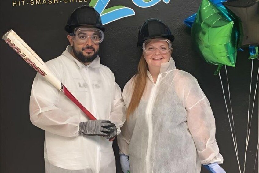 Two people in protective gear, one holding a cricket bat, and a backdrop with balloons and a logo. 3