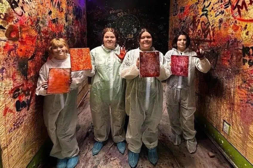 Four people in protective suits holding red panels in a graffiti-covered hallway. 5
