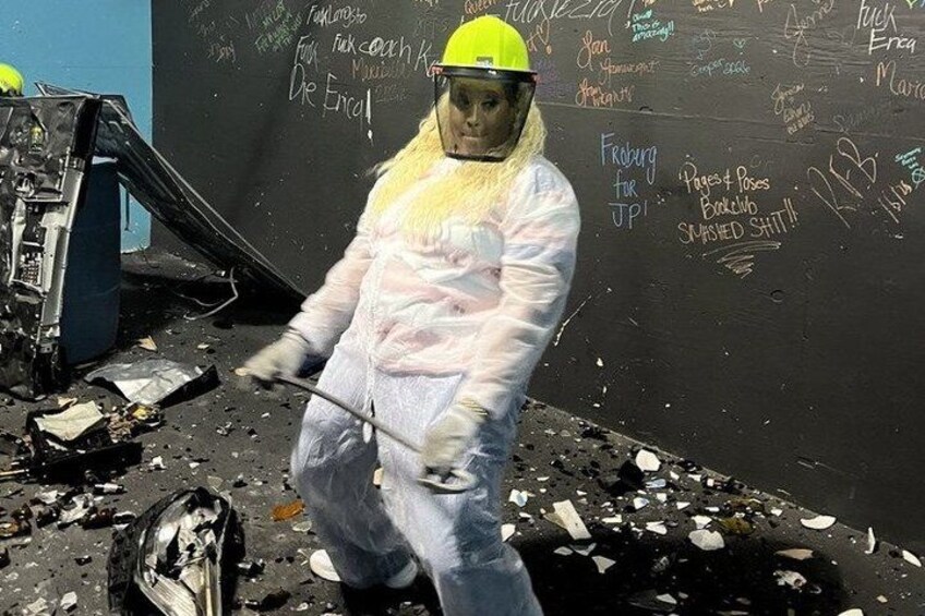 A person in protective gear cleaning debris from a damaged vehicle in a junkyard. 4