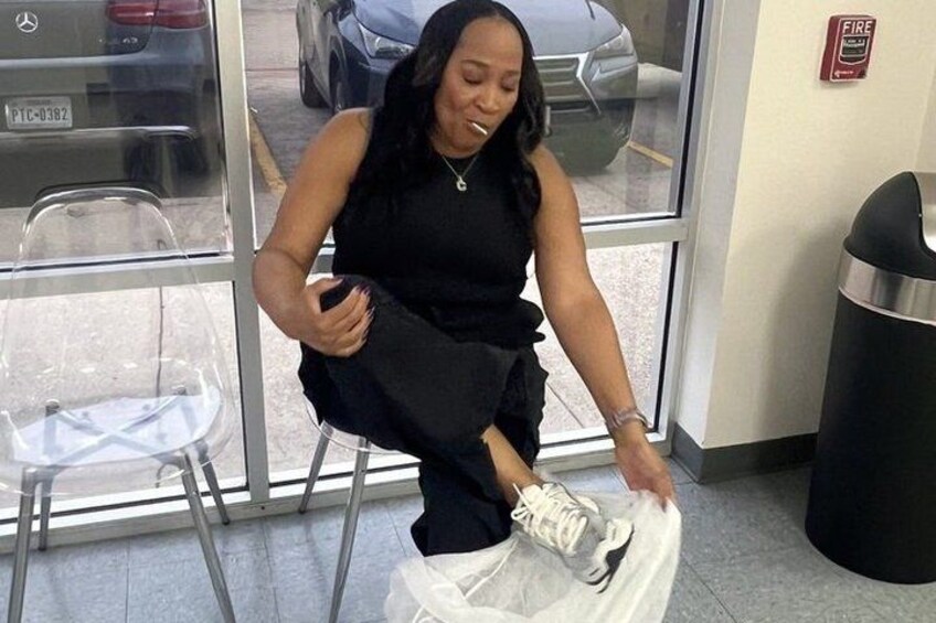 A person sitting on a chair, wearing a black outfit, and holding a white sneaker. 4
