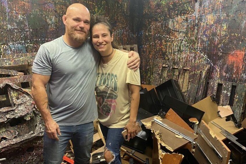 Two people standing in a cluttered room with wooden structures and paint splatters. 5