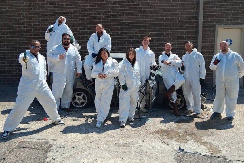 A group of people in white protective suits posing in front of a brick building. 1