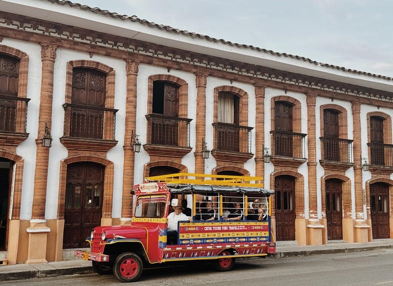 A colorful bus with passengers, parked in front of a historic building with ornate doors and windows. 1