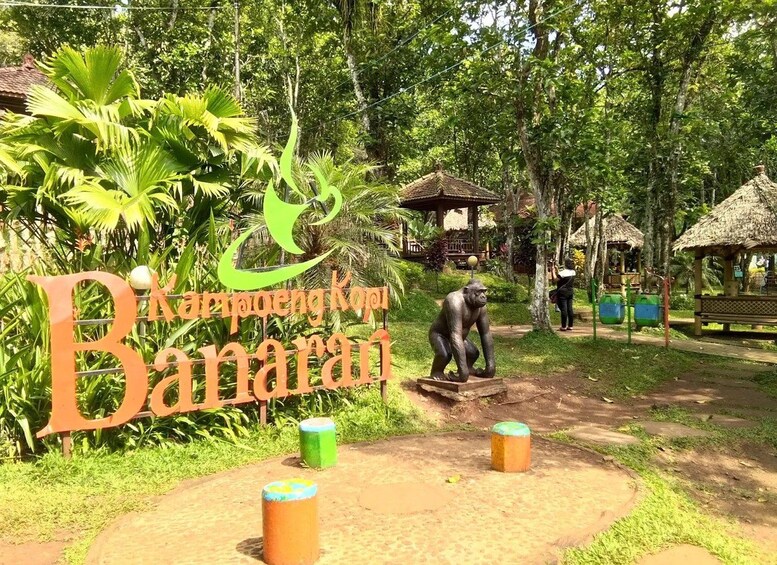 A park entrance with a large sign, a monkey statue, and a thatched-roof structure. 4