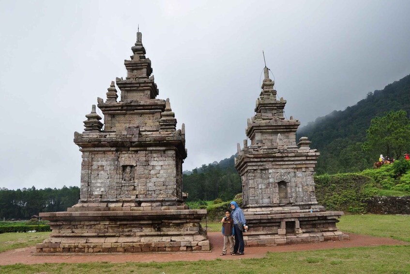 Two ancient stone structures with intricate carvings, surrounded by lush greenery and a mountainous backdrop. 2