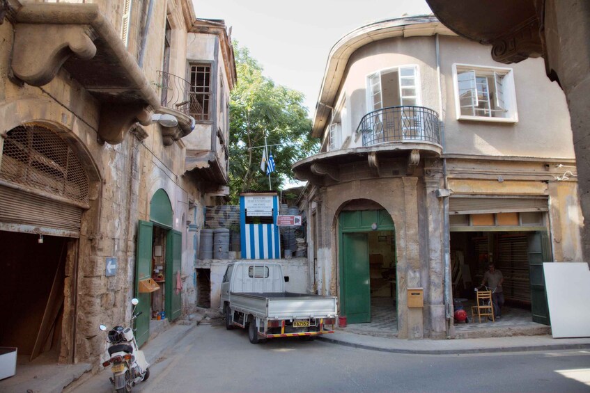 A narrow street with old buildings, a truck parked on the side, and a motorcycle. 1