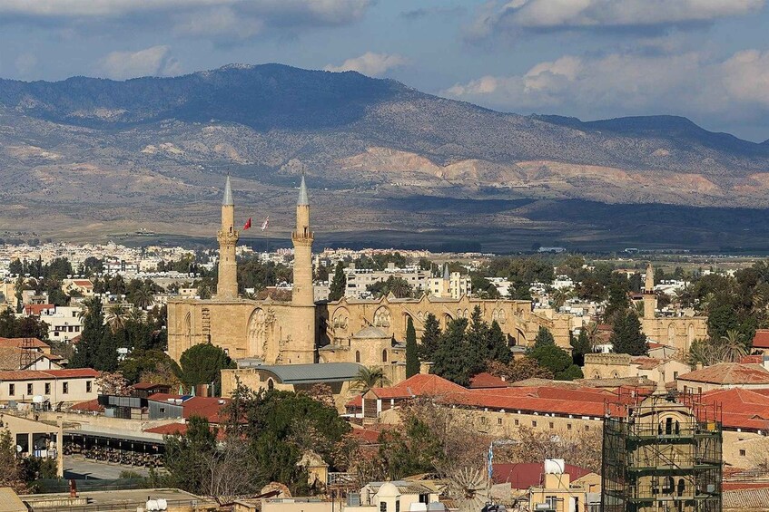 A cityscape with a prominent mosque featuring two minarets, surrounded by residential buildings and mountains in the background. 2