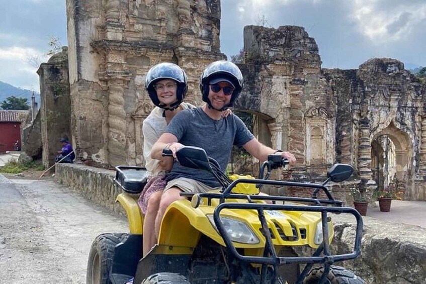 Two people on a yellow ATV with a historic stone structure in the background. 4