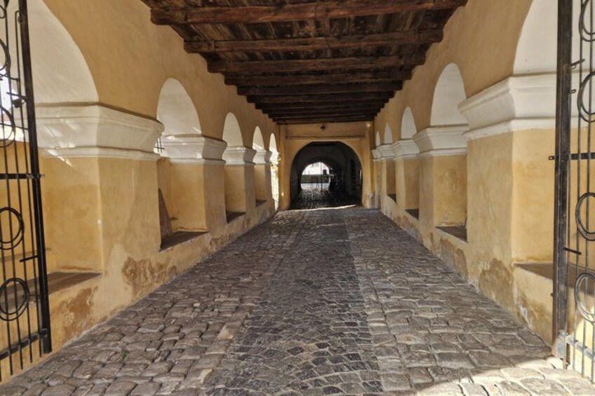 A cobblestone pathway with arches and a wooden ceiling. 4