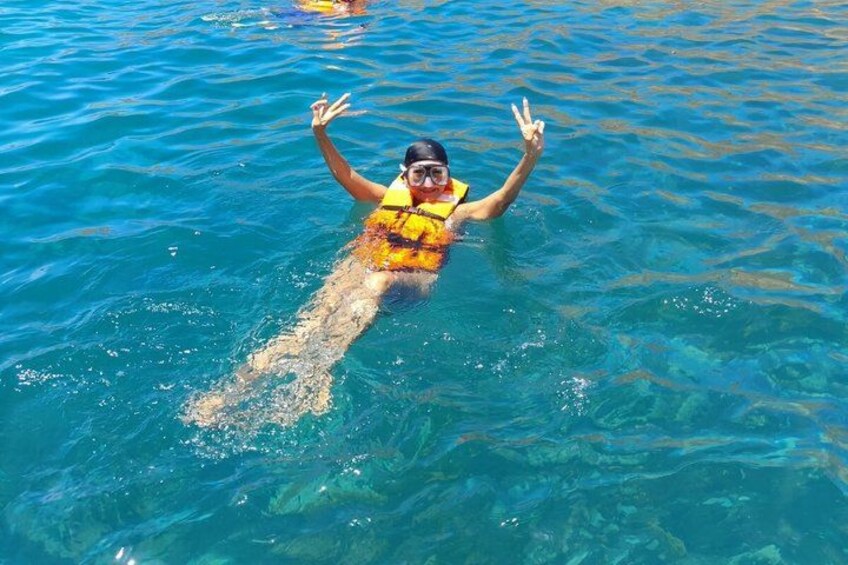 A person swimming in clear blue water, wearing a yellow life jacket. 3