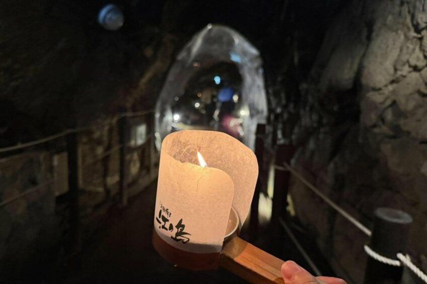 A hand holding a lit candle with Chinese characters, in a dimly lit cave with rocky walls. 2