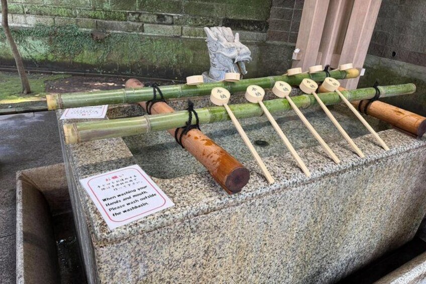 A stone basin with wooden sticks and a sign instructing to wash hands before entering. 5