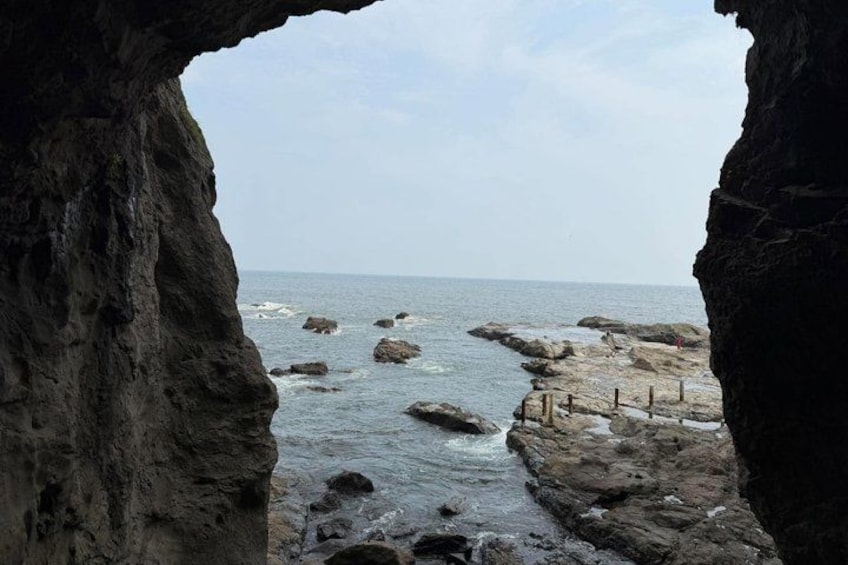 A rocky coastline with a cave entrance, waves crashing against the rocks, and a clear sky. 4