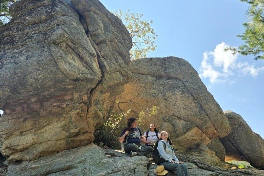 Two people sitting on a rock formation with a large boulder in the background. 1
