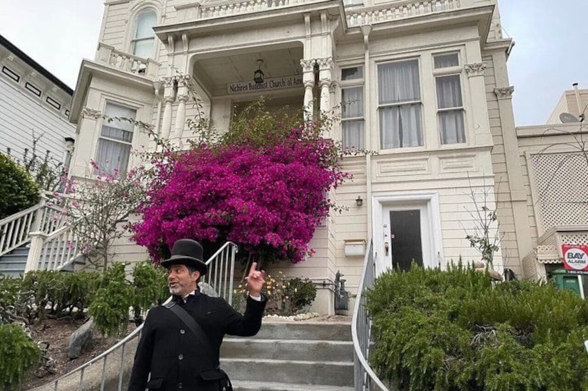 A person in a black uniform standing in front of a building with a large pink flowering tree. 2