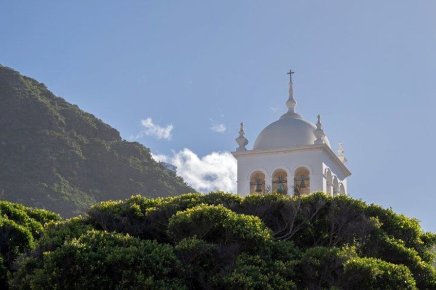 A white church with a dome and cross, surrounded by lush green trees and a mountain in the background. 5