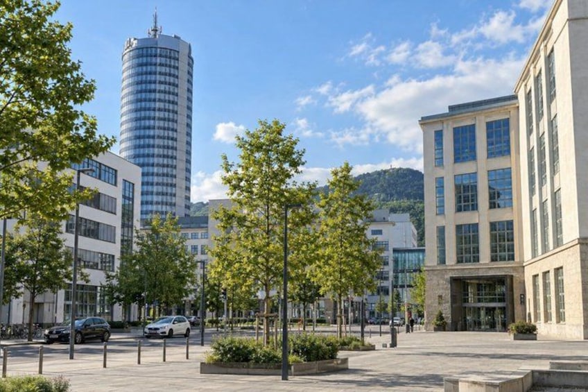 A city street with modern buildings, a tall cylindrical structure, and trees. 2