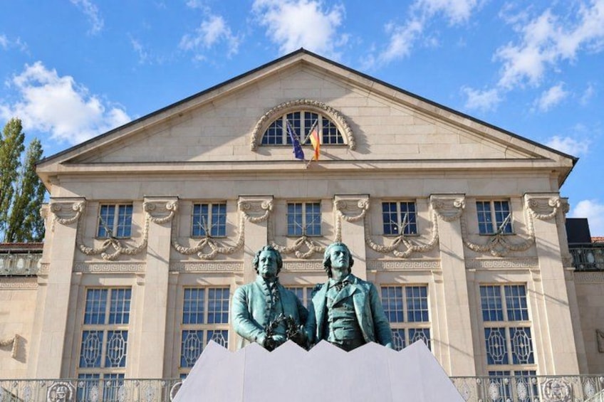 A neoclassical building with a central pediment, two statues, and a flag. 4