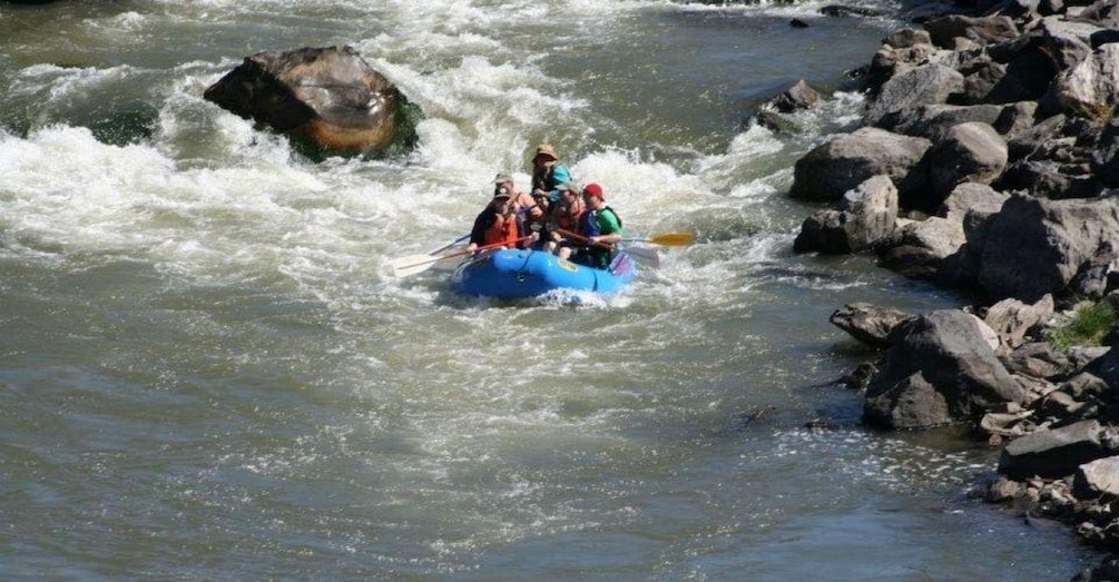 A group of people rafting down a river with rocks and rapids. 1