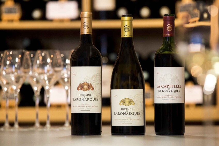 Three bottles of Domaine de Baronarques wine on a bar counter with glasses in the background. 1