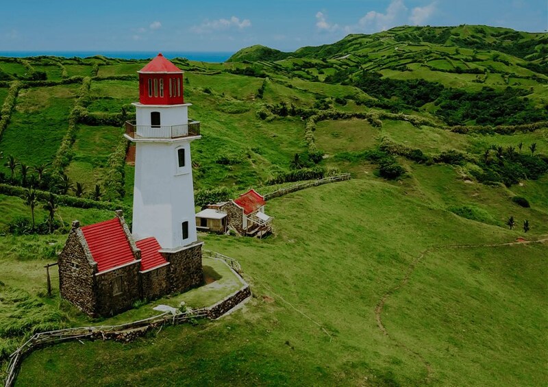 A white lighthouse with a red roof, surrounded by lush green fields and hills. 3