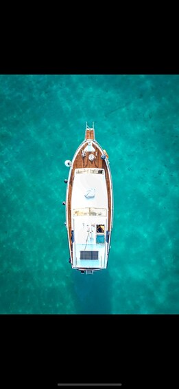 An aerial view of a boat with a wooden deck and a cabin, floating on clear turquoise water. 1