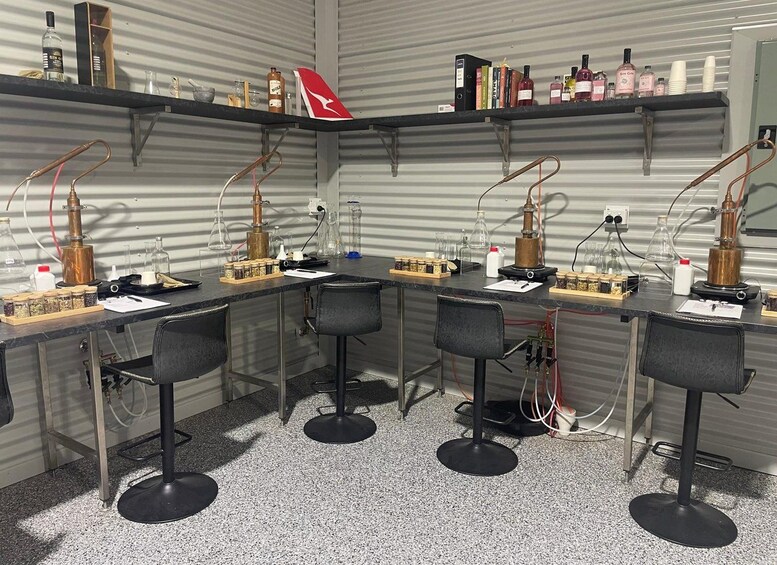 A laboratory with multiple workstations, each equipped with a distillation apparatus, flasks, and various chemicals. Shelves above contain books and bottles. 2