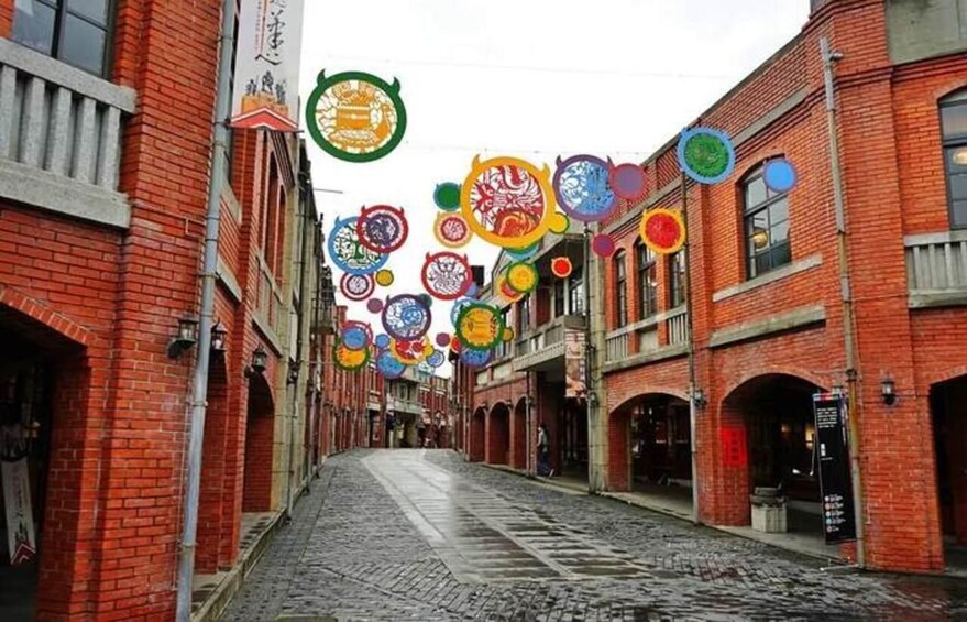 A street with red brick buildings, cobblestone pavement, and colorful circular decorations hanging from the ceiling. 2