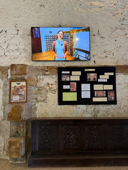 Una pared con una pantalla de televisión, un tablón de anuncios con texto e imágenes, y un cuadro enmarcado. 2