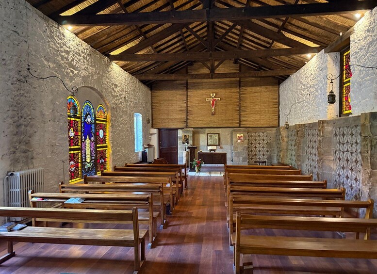 Interior de iglesia con bancos de madera, vidrieras, techo de madera y un crucifijo. 1