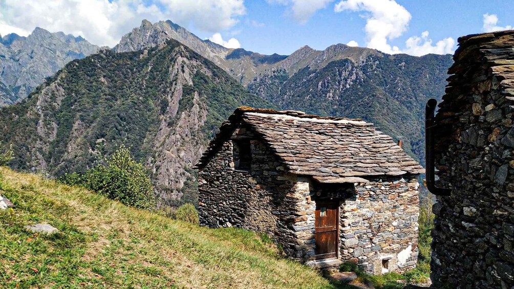 A stone cottage with a wooden door, surrounded by a mountainous landscape. 3
