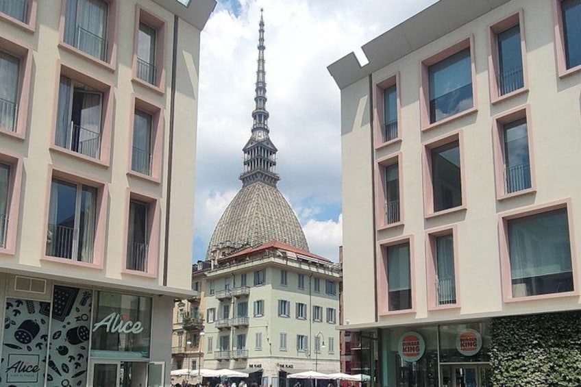 A building with a pointed spire, a shop with a sign reading 'Alice,' and a Burger King across the street. 1