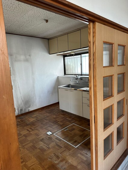 Una cocina con piso de madera, armarios blancos y una ventana con cortinas. 4