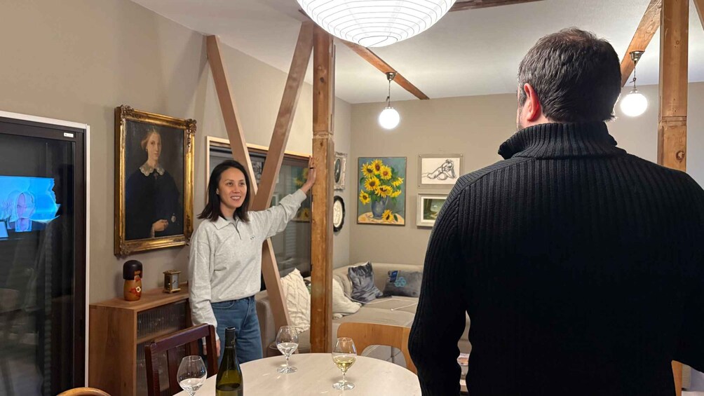 Una persona de pie en una habitación con un cuadro, una mesa con copas de vino y un ventilador de techo. 1