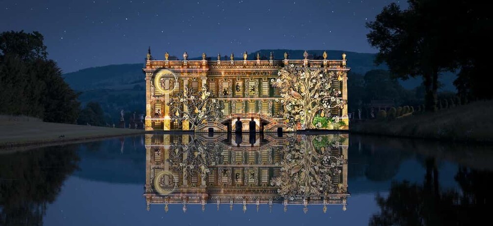 A grand illuminated building with a reflection in the water, surrounded by trees and hills. 1