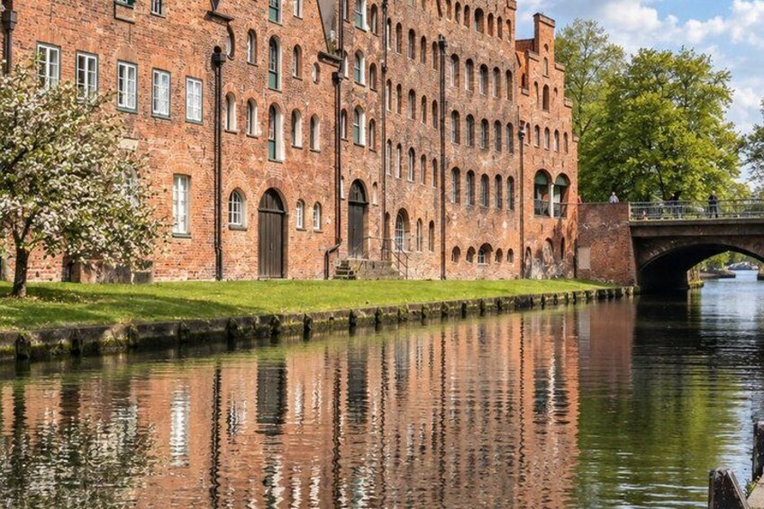 A large brick building with arched windows and a bridge over a calm river. 2