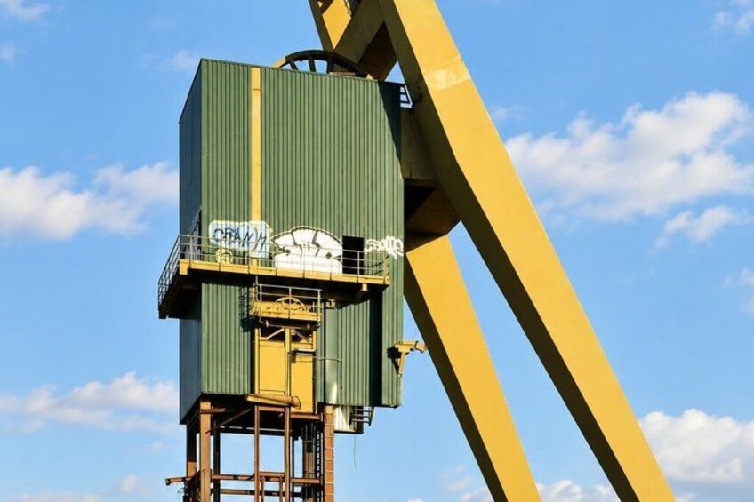 A green industrial structure with yellow support beams against a blue sky with clouds. 4
