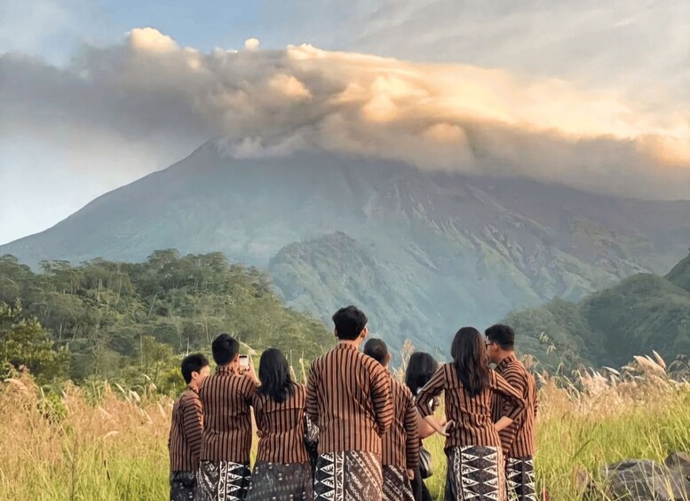 A group of people standing in a field, facing a mountain with a cloud above it. 5