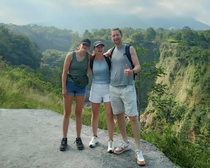 Three people standing on a rocky outcrop with a mountainous landscape in the background. 3