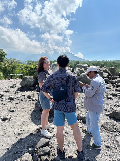 Three people standing on rocky terrain with a mountainous landscape in the background. 2