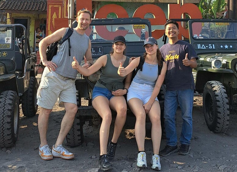 Four people posing in front of a vehicle with large tires and a logo. 4