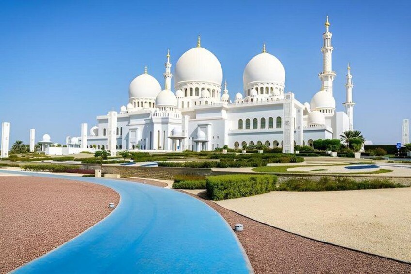 A large white mosque with multiple domes and minarets, surrounded by landscaped gardens and a blue water feature. 2